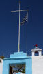 Symi - entrance and bell tower of Agios Emilianos monastery show the ubiquitous symbols in Greece - the cross and the national flag